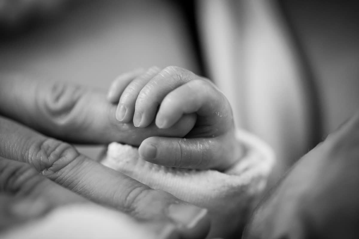 Parto humanizado - bebê recém nascido segurando o dedo de um adulto em preto e branco.