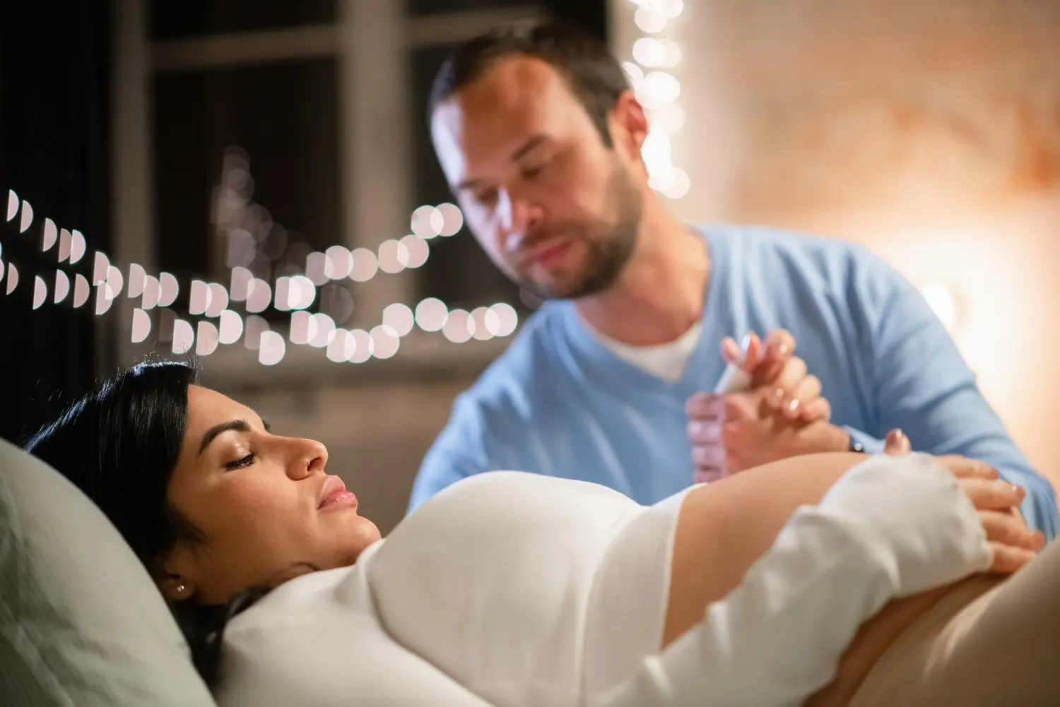 Mulher grávida deitada, segurando as mãos de um homem, com a expressão de que está com sintomas do trabalho de parto