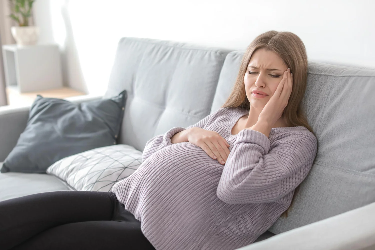 Mulher sentada no sofá, sofrendo com a azia na gravidez