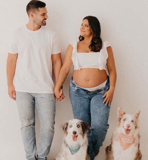 Mulher grávida de mãos dadas com o marido e seu cachorros ao lado