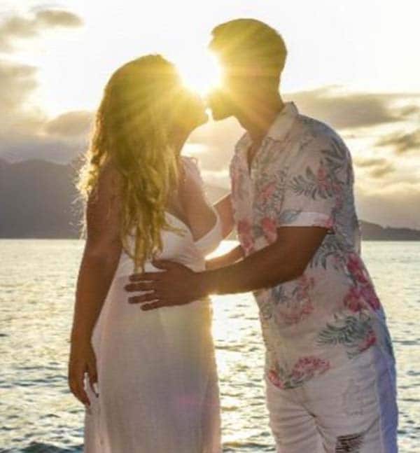Mulher grávida beijando o marido na praia.