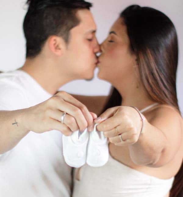 Casal se beijando segurando sapatinhos do bebê a caminho